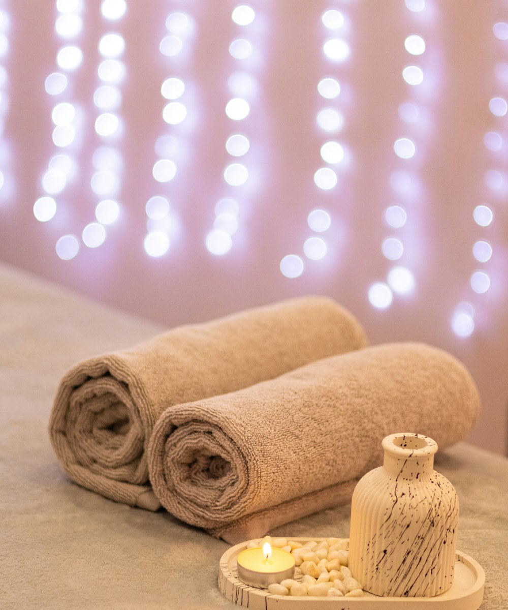 Toallas enrolladas, una vela encendida y un difusor en un ambiente de spa
